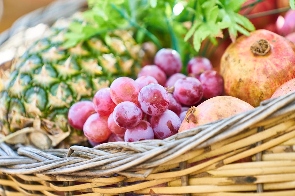 A colorful mix of fresh fruits including grapes, pineapple, and pomegranates in a wicker basket.